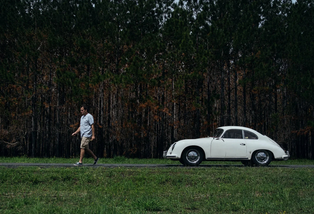 James Corbett walking beside the antique white Porsche 356A, seen in side profile.