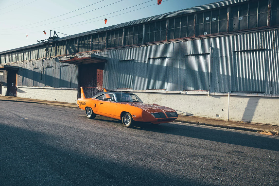 Orange 1970 Plymouth Super Bird beside an industrial warehouse